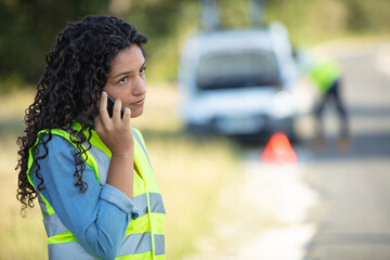 young female driver wearing a high visibility vest calling assistance