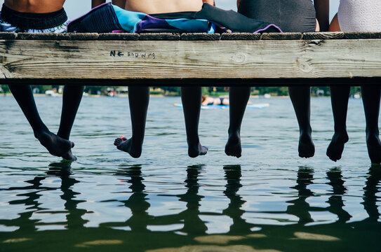 four teenagers sit at the end of a dock, legs and feet edition