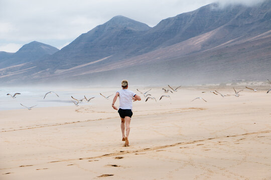 Young man running with birds in a paradisiacal beach