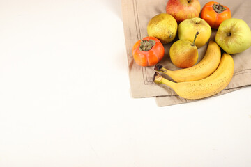 bananas apples pears persimmon on a linen tablecloth on a white background