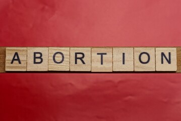 text the word abortion from gray wooden small letters with black font on an red table