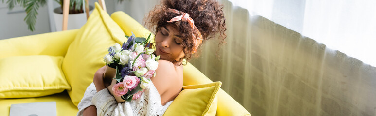 horizontal image of young woman with closed eyes holding bouquet and smelling flowers in living room