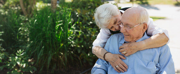 Happy, fun loving elderly couple outside in garden using wheelchair