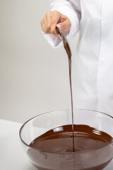 Close up making organic hand-crafted chocolate, pouring dark melted chocolate on isolated white background. Chocolatier preparing pralines, chocolate candy, truffle. Pastry bakery patisserie concept