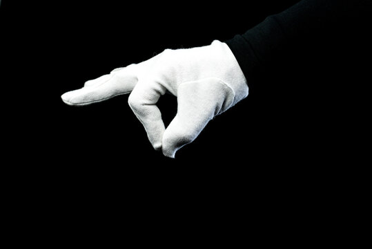 A hand wearing white glove on black background