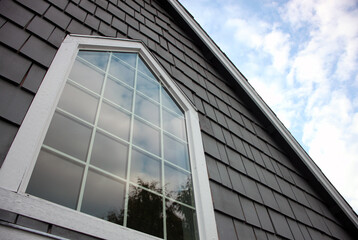 Fototapeta na wymiar Large window with cloud reflections surrounded by white trim and gray shingles