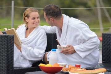 couple in bathrobes sat outdoors embracing at breakfast time