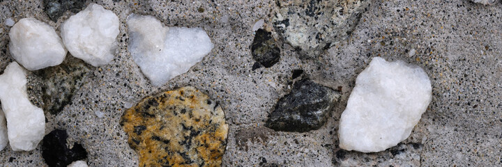 Concrete wall texture with pebbles. Decorative rough concrete surface with white, black and gray stones. Wide panoramic texture for background and design.