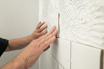 Man laying white tiles in bathroom shower
