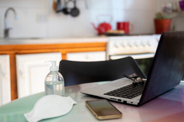 
notbook on a table in a home kitchen, with alcohol gel, cell phone, a cup and chinstrap