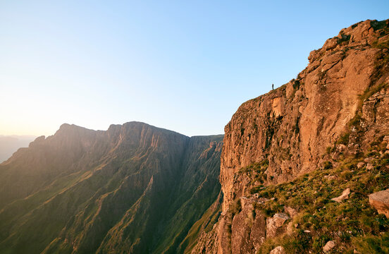 Hiker standing on a mountain cliff edge at sunrise.