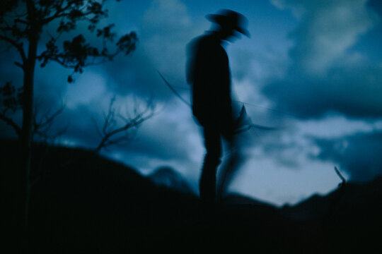 one adult male walks with bow and arrow at dusk in the forest