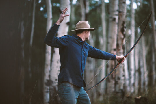 Adult male archer shoots a bow and arrow in the forest at dusk