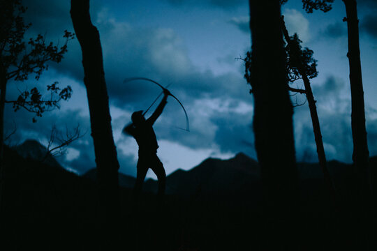 one adult male shoots bow and arrow at dusk in the forest