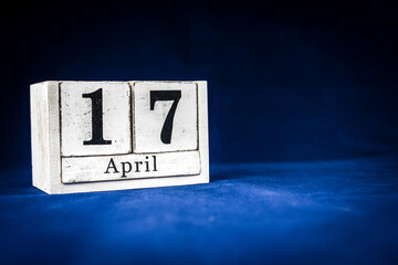 April 17th, Seventeenth of April, Day 17 of month April - rustic wooden white calendar blocks on dark blue background with empty space for text.
