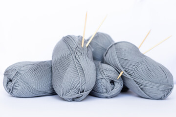 Many gray balls of thread on a white background. The threads and knitting needles lie on the background. We knit as a gift. Home crafts. Knitting hobby