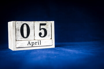 April 5th, Fifth of April, Day 5 of month April - rustic wooden white calendar blocks on dark blue background with empty space for text.