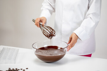 Closeup female chef stirring and pouring dark melted chocolate with whisk isolated on white...