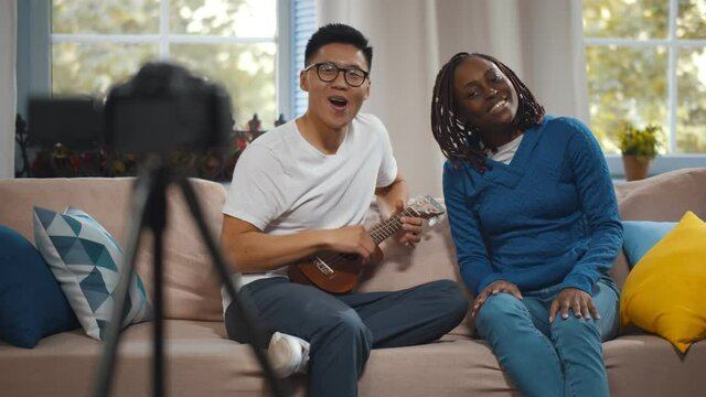 Young Multiethnic Couple Recording Music Video Blog Sitting on Couch at Home