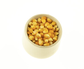 dried yellow corn seeds lie in a white ceramic bowl on an isolated background