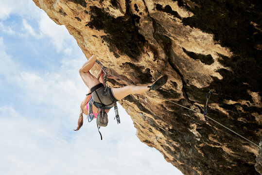 Unrecognizable woman in climbing gear ascending the cliff