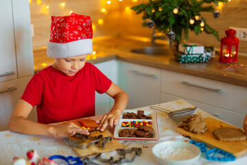 A boy in a santa hat prepares cookies in the kitchen. Form for Christmas gingerbread. Child in the kitchen in New Year's decor. Christmas cookies