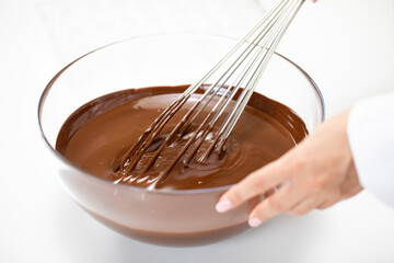Hand of confectioner mixing melted premium dark chocolate with whisk isolated on white. Melted Chocolate Swirls In glass Bowl. World Chocolate Day. Cooking video lessons. Culinary Blog concept