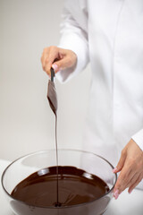 Closeup stirring and pouring dark melted chocolate isolated on white background. Chocolatier make organic bitter unsweetened hand-crafted chocolate. Candymaking, pastry production, dessert concept