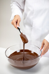 hand of Female Confectioner mixes melted milk chocolate in glass bowl. melted chocolate falls off spatula into pot. Preparation of premium handmade candies, truffles, chocolates and sweets.