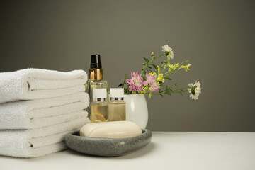 a shower set on the bedside table, clean white terry towels, several bottles of shower gel and shampoo, soap in a stone soap dish and a beautiful decorative bouquet of flowers