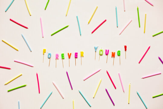 Forever young written with colourful birthday candles on pale peach background