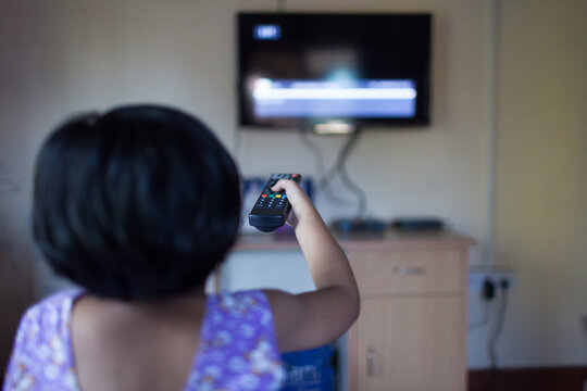 Little girl watching TV and changing channel with remote control