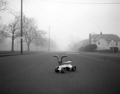 Fototapeta Black and white film photo of a child's toy in the middle of the street on a quiet, foggy morning.