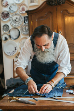 Environmental Indoor Portrait of Cool Senior Male Tailor Working on Living Room Table