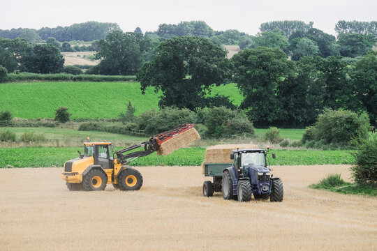 Wheel loader collecting straw bales and loading them onto a trac