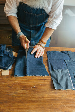 Close Up of Cool Senior Man Cutting Denim Fabric on Living Room Table
