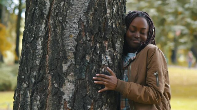 Casual cheerful african woman embracing tree in park