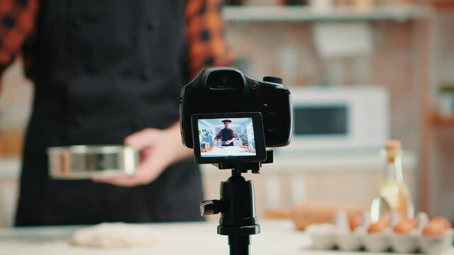 Close up of a video camera filming senior smiling man blogger in kitchen cooking. Retired blogger chef influencer using internet technology communicating on social media with digital equipment