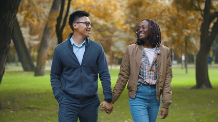 Portrait of happy multiethnic couple holding hands walking together in park - Powered by Adobe