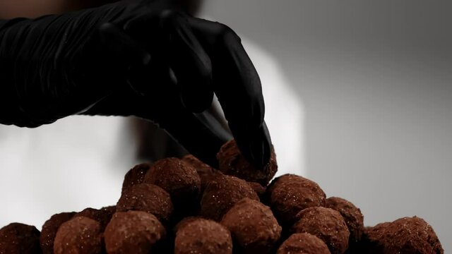 Confectioner's hand in black glove puts handmade truffle candy on top of sweets pile slow motion. Dolce vita concept. Luxury candies in golden dust. high society Elite lifestyle