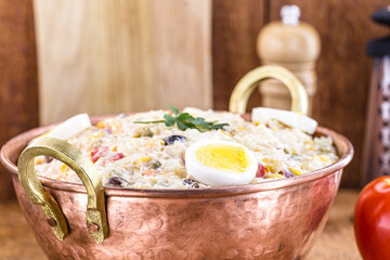 homemade mayonnaise with vegetables, eggs, tomatoes and fruits, typical Brazilian food, served in copper pot, isolated on rustic wooden background