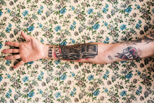 Tattooed male arm against of floral patterned wall