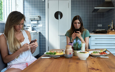 Two addictive girlfriends using their phones at breakfast table