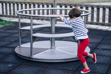 Side view of a little girl propelling a spinning carousel in a playground