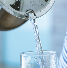 Naklejka na ściany i meble Uma pessoa enchendo um copo com água que está em uma jarra em alumínio. Conceito de vida saudável, bebida, água potável e hidratação.
