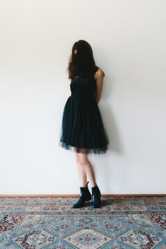 Movement shot of woman standing against a wall indoors, wearing party dress and plastic rain boots