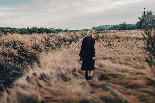 young blond woman in black clothes walking in the autumn field