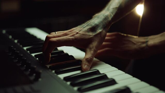 Unrecognizable person making music with keyboard in recording studio.