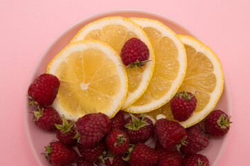 Fototapeta na wymiar lemon slices and raspberries in a pink plate on a pink background. Flat lay of tropical summer. Nutrition concept.Disease prevention.