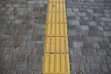 Yellow tactile tiles for the blind and visually impaired on the sidewalk in the city on the street